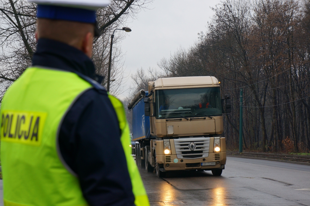 zdjęcie przedstawia: policjanta ruchu drogowego z samochodem ciężarowym w tle