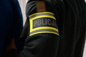 zdjęcie przedstawia: ręka policjanta z założoną opaską z napisem policja