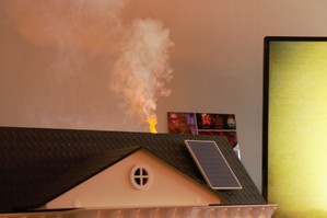 zdjęcie przedstawia: makietę domu i wydobywający się z komina dym