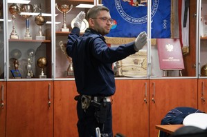 zdjęcie przedstawia: policjanta ruchu drogowego, który tłumaczy zasady kierowania ruchem podczas szkolenia strażaków
