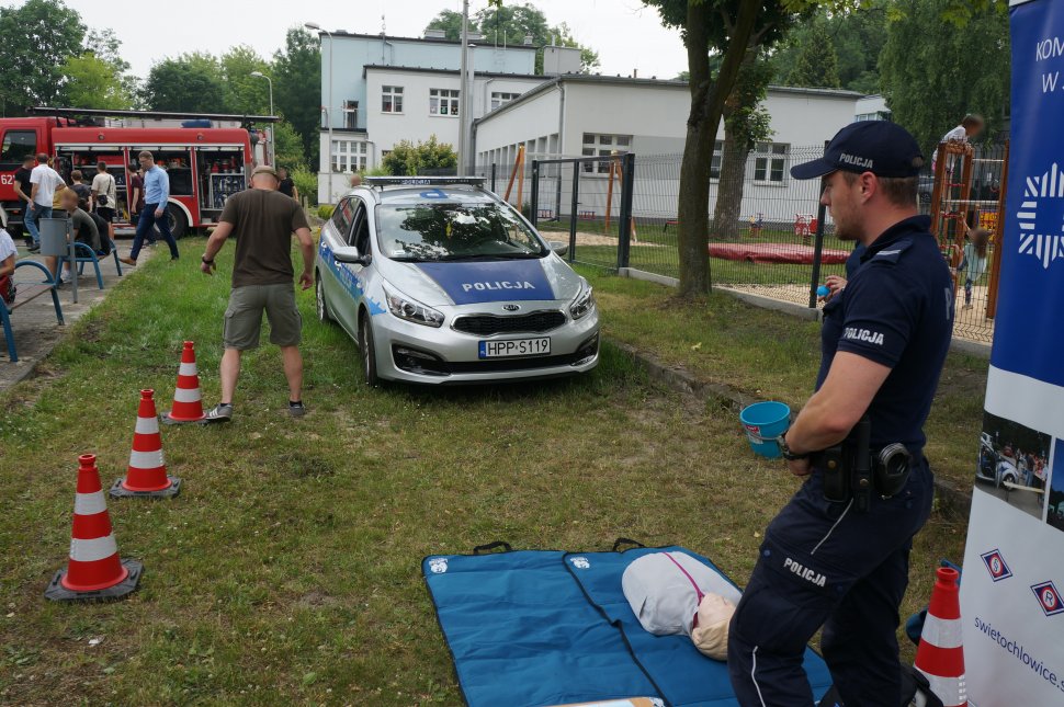 Na zdjęciu mundurowi przyglądają się jak jeden z uczestników próbuje pokonać tor przeszkód mając założone alkogogle, w tle widać innych uczestników festynu