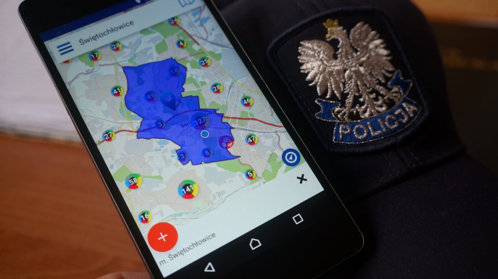 Na zdjęciu smartfon z otwartą aplikacją Krajowa Mapa Zagrożeń bezpieczeństwa, obok niego widac czapkę granatową z daszkiem z orłem na przodzie