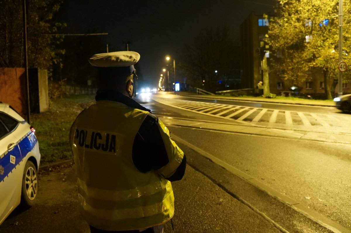 Na zdjęciu policjant z drogówki w trakcie obserwacji sytuacji na drodze po zmroku. Mundurowy zwraca uwagę na prawidłowe oświetlenie pojazdów.