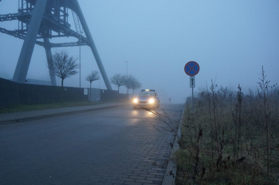 Na zdjęciu widać jadący, wyłaniąjący się zza gęstej mgłym radiowóz 