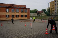 Zdjęcie przedstawia policjantów ruchu drogowego ustawiających tor przeszkód dla dzieci, które przystąpiły do egzaminu na kartę rowerową.