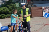 Na zdjęciu policjant WRD wręczający odblaskową opaskę na rękę rowerzyście, który ukończył tor przeszkód.