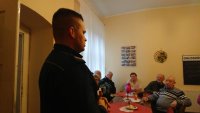 Na pierwszym planie zdjęcia dzielnicowy, w tle grupa seniorów siedząca przy stole.