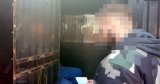 Na pierwszym planie zdjęcia policjant kryminalny, w tle osoba zatrzymana siedząca w policyjnym radiowozie.