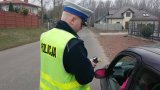 Policjant Wydziału Ruchu Drogowego dokonujący kontroli stanu trzeźwości kierowcy siedzącego w pojeździe z prawej strony zdjęcia.