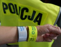 napis policja w tle, ręka z dwoma opaskami odblaskowymi