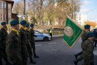 przemarsz uczestników  pod Muzeum Powstań Śląskich, w tle policjanci zabezpieczający uroczystość