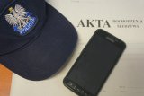 czapka policyjna położona na teczce z napisem akta dochodzenie/śledztwo, obok telefon komórkowy