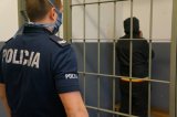 zatrzymany mężczyzna w pomieszczeniu dla osób zatrzymanych na pierwszym planie policjant nadzorujący zatrzymanego