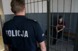 mężczyzna oczekujący w pomieszczeniu dla osób zatrzymanych pod nadzorem umundurowanego policjanta