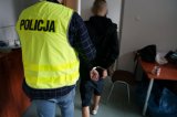 zatrzymany mężczyzna zakuty w kajdanki podczas doprowadzenia przez policjanta z wydziału kryminalnego na przesłuchanie w jednostce policji