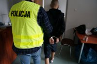 zatrzymany mężczyzna zakuty w kajdanki podczas doprowadzenia przez policjanta z wydziału kryminalnego na przesłuchanie w jednostce policji