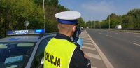 Na zdjęciu policjant Wydziału Ruchu Drogowego stoi obok radiowozu i kontroluje prędkość