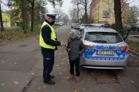 umundurowany policjant z drogowki podczas przekazywania opaski odblaskowej dziecku w trakcie działań &quot;Bezpieczny pieszy&quot;