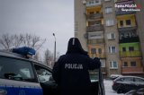 na zdjęciu policjant stojący obok radiowozu, w tle blok mieszkalny