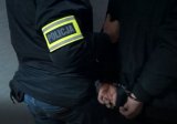 nieumundurowany policjant w trakcie prowadzenia zatrzymanego mężczyzny zakutego w kajdanki na rece trzymane z tyłu