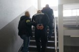 nieumundurowani policjanci podczas prowadzenia zatrzymanego mężczyznę zakutego w kajdanki na rękach z tyłu