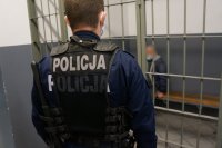 umundurowany policjant na tle policyjnej celi podczas nadzorowania zatrzymanego meżczyzny