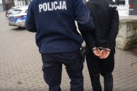 mundurowy podczas prowadzenia do jednostki policji zatrzymanego mężczyznę zakutego w kajdanki na ręce trzymane z tyłu