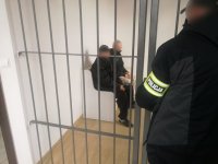 na zdjęciu nieumundurowany policjant w trakcie nadzorowania w policyjnej celi dwóch zatrzymanych mężczyzn