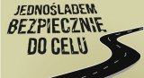 Czarny napis Jednośladem bezpiecznie do celu, w tle fragment drogi