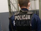 Mundurowy stający twarzą do policyjnej celi, ubrany w kamizelkę taktyczną z napisem Policja