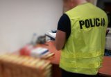 Na zdjęciu nieumundurowany policjant w kamizelce odblaskowej z napisem policja podczas prowadzenia oględzin zabezpieczonej kontrabandy w postaci paczek z papierosami