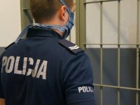 Policjant stojący tyłem na tle kraty z pomieszczenia dla osób zatrzymanych