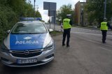 Na zdjęciu radiowóz policyjny przy którym stoi umundurowany policjant. Po prawej stronie widać drugiego mundurowego który przygotowuje się do zatrzymania pojazdu do kontroli drogowej.