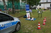 stoisko mundurowych z miejscowej policji na którym został przygotowany radiowóz do pokazu, fantom do ćwiczenia pierwszej pomocy, stół z materiałami promującymi bezpieczeństwo. W oddali widać stroiska innych uczestników festynu