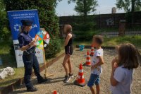 Na zdjęciu mundurowa, która stroi przy kole wiedzy z listą pytań, obok stoją dzieci czekające w kolejnce do zakręcenia kołem aby odpowiedzieć na pytania związane z bezpieczeństwem