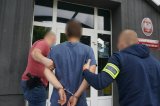 Na zdjęciu nieumundurowani policjanci prowadzą do budynku świętochłowickiej komendy zatrzymanego mężczyznę zakutego w kajdani na ręce trzymane z tyłu