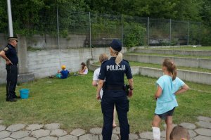 Na zdjeciu widac mundurową oraz strażnika miejskiego, którzy wraz z innymi dziećmi dopingują uczestników którzy probują założyć jak najszybciej buty.