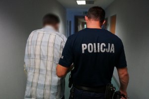 Na zdjęciu zatrzymany mężczyzna prowadzony na przesłuchanie przez umundurowanego policjanta