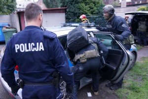 Na zdjęciu widać policjanta oraz  funkcjonariuszy Samodzielnego Pododdziału Kontrterorystycznego Policji po umieszczeniu w radiowozie zatrzymanego mężczyzny, który jest sprawdzany pod kątem posiadania niebezpiecznych narzędzi