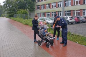 Mundurowy w trakcie rozmowy z rodzicami w dniu rozpoczęcia roku szkolenego w jednej ze świętochłowickich szkół. Na zdjęciu widać jak mundurowy przekazuje dzieciom gadżety związane z bezpieczeństwem