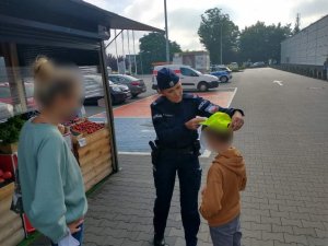 Na zdjęciu mundurowa zakłada na głowę chłopca czaspkę odblaskową z kampanii Mamo! Tato ! Tutaj jestem. Na zdjęciu widać także stojącą obok mamę chłopca