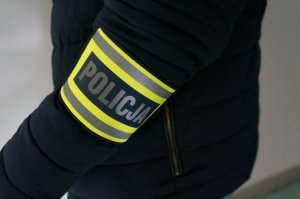 Na zjęciu zbliżenie na opaskę odblaskową z napisem policja na ramieniu nieumundurowanego policjanta