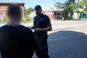 Na zdjęciu widać umundurowanego policjanta w trakcie prowadzenia czynności legitymowania wobec pieszego