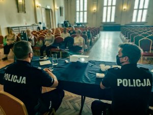 Na pierwszym planie mundurowi siedzący tyłem do obiektywu, prowadzą wykład na temat oszytw. W tle widac siedzacych seniorów, przysłuchujących się prowadzonej prelekcji