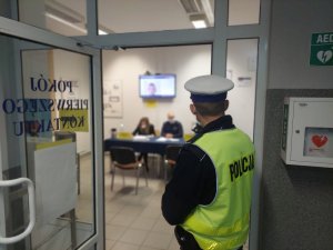 Na zdjęciu widać wnętrze świętochłowickiej komendy. Na pierwszym planie widać policjanta ze słuzby porzadkowo ochronnej. W tle widać stanowiska należącego do punktu Kontrolno-Informacyjnego i wyznaczonych do obsługi policjantów.