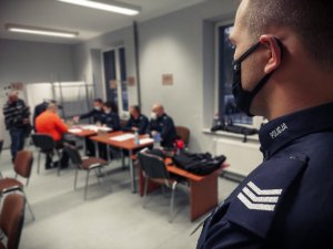 Na zdjęciu zbliżenie na pagon policjanta ze słuzbży porządkowo ochronnej. W tle widać obsługę oraz punkt wydawania wyposażenia