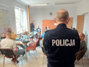 Na zdjęciu widać napis Policja na bluzie obserwatora, w tle widać rezerwistów siedzących na jadalni