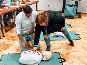 Na zdjeciu rezerwista klęczący przy fantomie oraz prowadząca wykład dotyczący  pierwszej pomocy. Kobieta pokazuje wskazując na fantomie właściwie miejsce wykonywania uciśnięć przy masażu serca