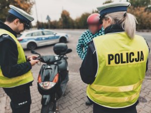 Na zdjeciu policjanci z dorgówki w trakcie prowadzenia kontroli drogowej kierującego motorowerem. W tle widać policyjny radiowóz