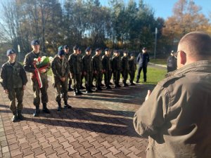 Na zdjeciu widać Przedstawiciela Stowarzyszenia Rodzina Policyjna 1939 r. przed Grobem Nieznanego Policjanta Polskiego znajdującym się przy siedzibie śląskiej Policji. W tle widać stojących w dwu szeregu kadetów. Przed nimi troje uczniow ustawionych w poczet honorowy z wiązanką kwiatów w rękach.